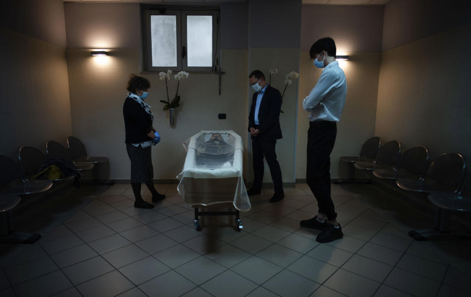 Sabatino Di Girolamo, center, mayor of Roseto degli Abruzzi, with his son Francesco, right, and his sister Marisa Di Felice, mourns his mother Annunziata, laid in state in the morgue of the Giuseppe Mazzini Hospital in Teramo, central Italy, Tuesday, May 12, 2020. Under new regulations imposed by the COVID-19 pandemic only three people wearing face masks could be allowed inside the morgue to respect the distancing requirements. With no comfort from relatives and friends, they wept alone in an unreal solitude. (AP Photo/Domenico Stinellis)