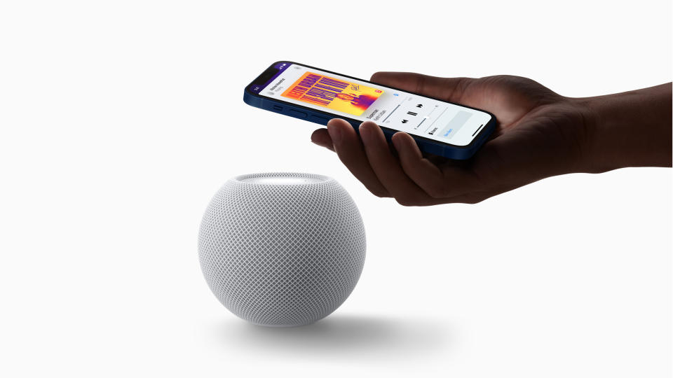 Someone holding an iPhone displaying Apple Music above an Apple HomePod smart speaker.