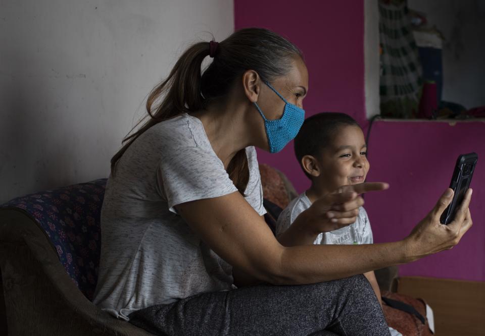 In this April 27, 2020 photo, 5-year-old Daniel sits with his grandmother as they chat via a messenger service with his father Misael Cocho, who fled Venezuela to work in Peru, in their apartment in Caracas, Venezuela. Perez said the highlights of her days are the text messages from her son, who also calls every few days so the Daniel can hear his father's voice. (AP Photo/Ariana Cubillos)