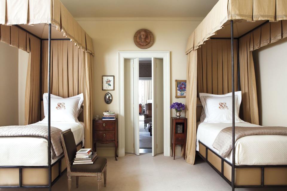 bedroom with matching iron beds with canopies and curtains of a cotton silk and an antique side tables are italian and french, and the chair and a double door opening out and a wooden medallion figure over it