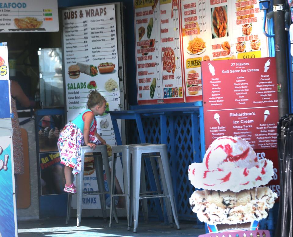 A little girl crawls up onto a stool as her mom and her get ice cream on a hot afternoon at Hampton Beach Wednesday.