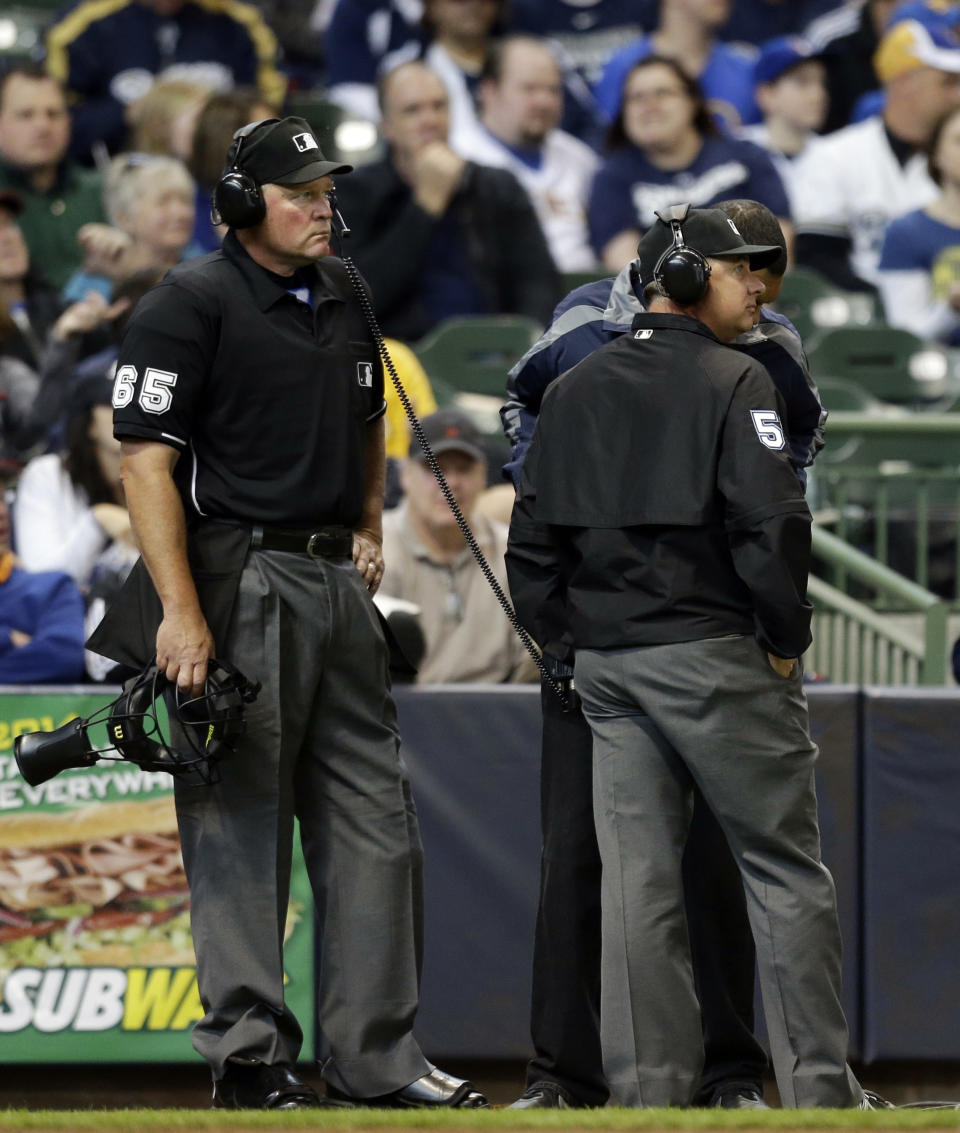 Umpire Ted Barrett (65) listens to the central replay booth in New York in the sixth inning of an opening day baseball game between the Atlanta Braves and Milwaukee Brewers, Monday, March 31, 2014, in Milwaukee. An umpire's call has been overturned for the first time under Major League Baseball's expanded replay system, with Brewers' Ryan Braun ruled out instead of safe. (AP Photo/Jeffrey Phelps)