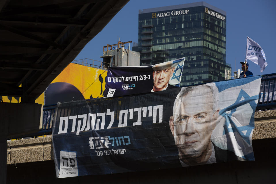 Blue and White party activist waves a flag behind an election campaign billboard that shows the party's leader Benny Gantz, in Tel Aviv, Israel, Sunday, March. 1, 2020. Israel heads into its third election in less than a year on Monday, March 2nd. Hebrew on billboard reads,"must move forward". (AP Photo/Oded Balilty)