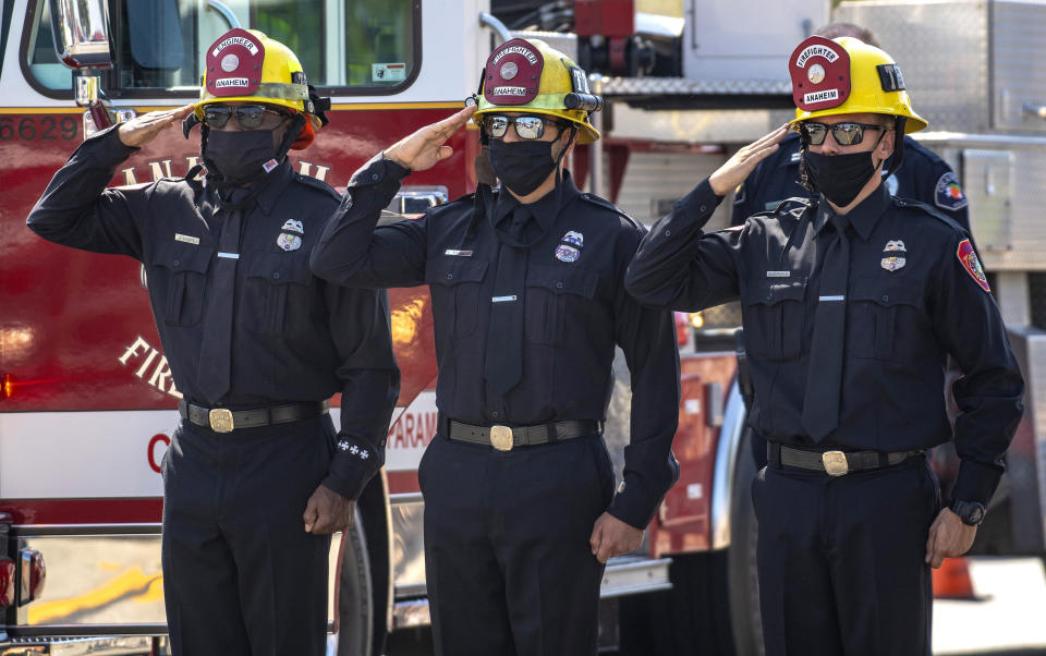 Anaheim firefighters salute as the procession carrying fallen firefighter Charles Morton, killed while battling a blaze in the mountains east of Los Angeles, along Hewes Street in Orange, Calif., Tuesday, Sept. 22, 2020, from San Bernardino to the Ferrara Colonial Mortuary in Orange. Morton, 39, a San Diego native, was a 14-year veteran of the U.S. Forest Service and a squad boss for the Big Bear Interagency Hotshots in San Bernardino National Forest, officials said. (Mark Rightmire/The Orange County Register via AP)