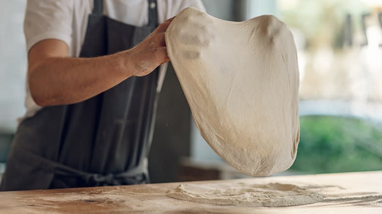hands stretching homemade pizza dough over flour pile