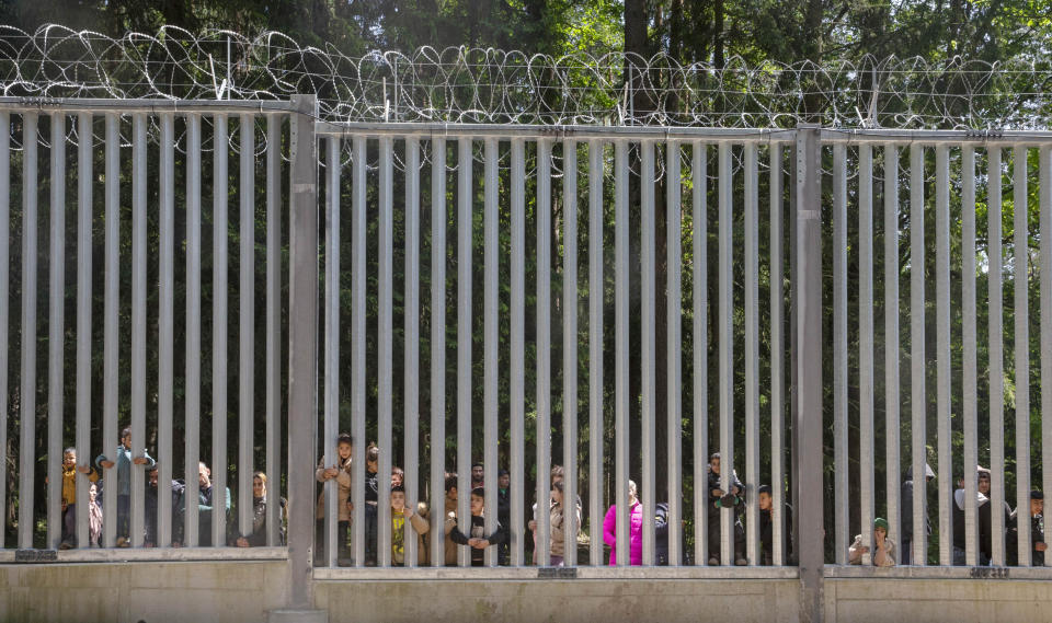 Members of a group of some 30 migrants seeking asylum are seen in Bialowieza, Poland, on Sunday, 28 May 2023 across a wall that Poland has built on its border with Belarus to stop massive migrant pressure. The group has remained stuck at the spot for three days, according to human rights activists. (AP Photo/Agnieszka Sadowska)