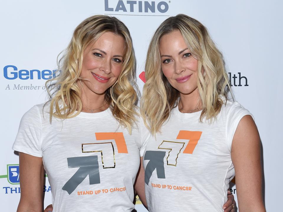 brittany and cynthia daniel, near identical-looking adult women twins, stand at a stand up to cancer read carpet smiling