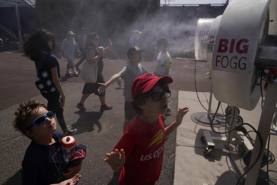 Brothers Henry Peters, 6, left, and Charles Peters, 8, cool off in misting fans at the USTA Billie Jean King National Tennis Center in New York, Tuesday, Aug. 22, 2023. An Associated Press analysis shows the average high temperatures during the U.S. Open and the three other Grand Slam tennis tournaments steadily have grown hotter and more dangerous in recent decades. (AP Photo/Seth Wenig)