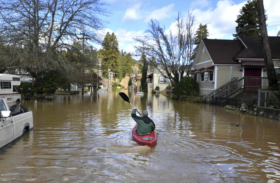 A kayak paddles down a flooded street past a pickup truck whose wheels are half-submerged.