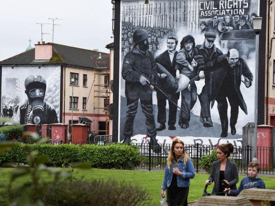 A family walks past a mural in Derry depicting a scene from Bloody Sunday (Getty)