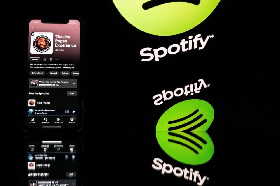This picture taken in Toulouse, southwestern France, on January 31, 2022 shows a smartphone displaying the Joe Rogan podcast and a screen displaying the Spotify&#39;s logo. - Caught in a disinformation maelstrom, Spotify announces it will guide listeners of Covid-19 podcasts to established facts about the pandemic. This comes after artists pulled their songs in protest at the platform given on Spotify to podcaster Joe Rogan, accused of spreading damaging myths about the pandemic. (Photo by Lionel BONAVENTURE / AFP) (Photo by LIONEL BONAVENTURE/AFP via Getty Images)