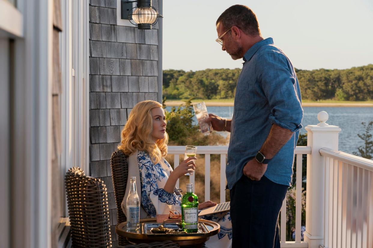 lev schreiber and nicole kidman holding up glasses with alcohol inside while sitting and standing on a porch overlooking the bay