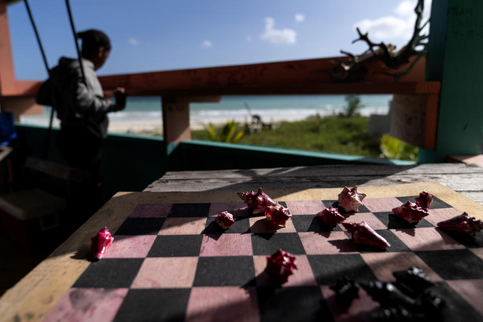 Small conch shells serve as game pieces on a checkers board as a young girl sits on a swing at a restaurant in Pelican Point, Grand Bahama Island, Bahamas, Saturday, Dec. 3, 2022. The shellfish appears prominently at the top of the national coat of arms and conch is widely recognized as the national dish. Symbols of the shellfish are everywhere. Conch shells serve as paperweights, bowls, musical instruments and Christmas ornaments. (AP Photo/David Goldman)