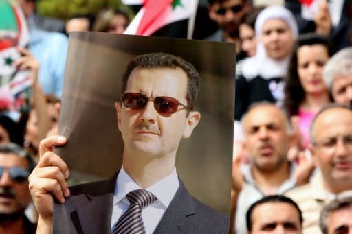 A Syrian protestor holds up a picture of President Bashar al-Assad during a pro-government demonstration outside the Syrian Central Bank in Damascus. Twin blasts targeting security buildings killed more than 20 people in the northwest Syrian city of Idlib, a monitoring group said, as the chief UN monitor presses both sides to end more than 13 months of violence