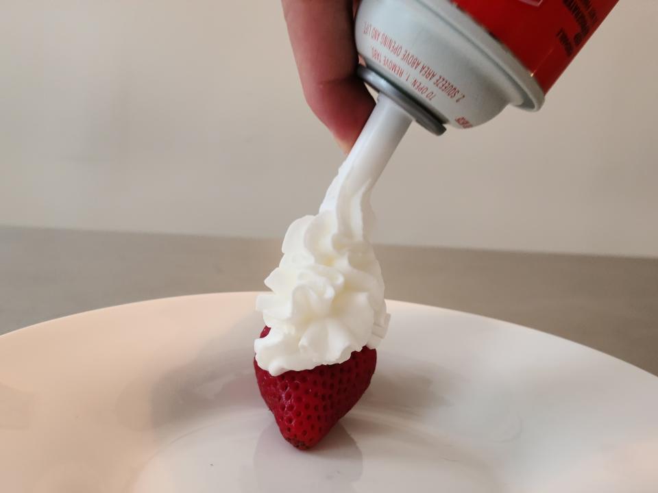 hand spraying can of krasdale whipped cream onto a strawberry