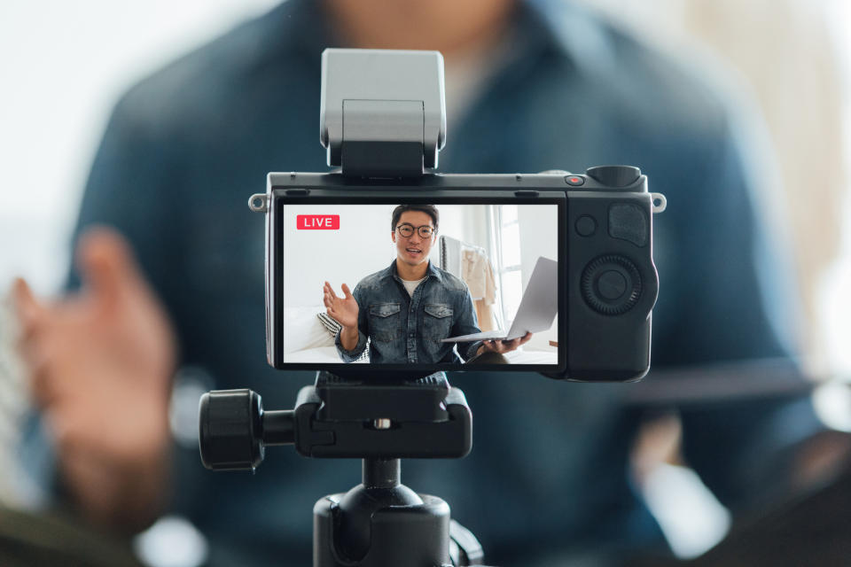 Copped shot of confident young man talking while filming through video camera for vlogging at home.