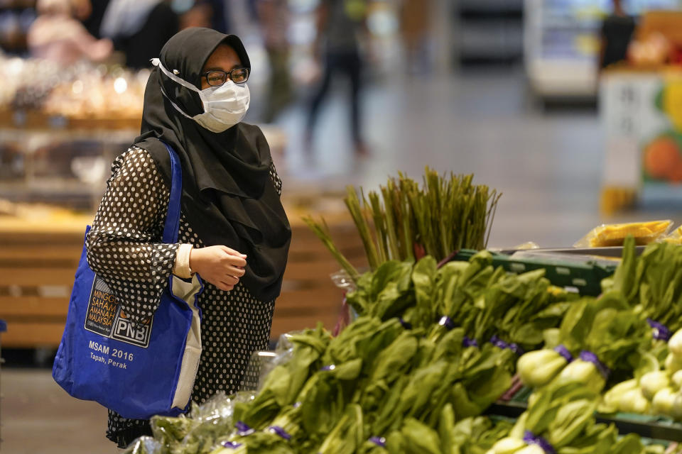 A shopper wearing a face mask to help curb the spread of the coronavirus looks at produce and a grocery in Putrajaya, Malaysia, Monday, Oct. 5, 2020. Prime Minister Muhyiddin Yassin says he will self-quarantine after a Cabinet minister he was in contact with tested positive for the coronavirus. (AP Photo/Vincent Thian)