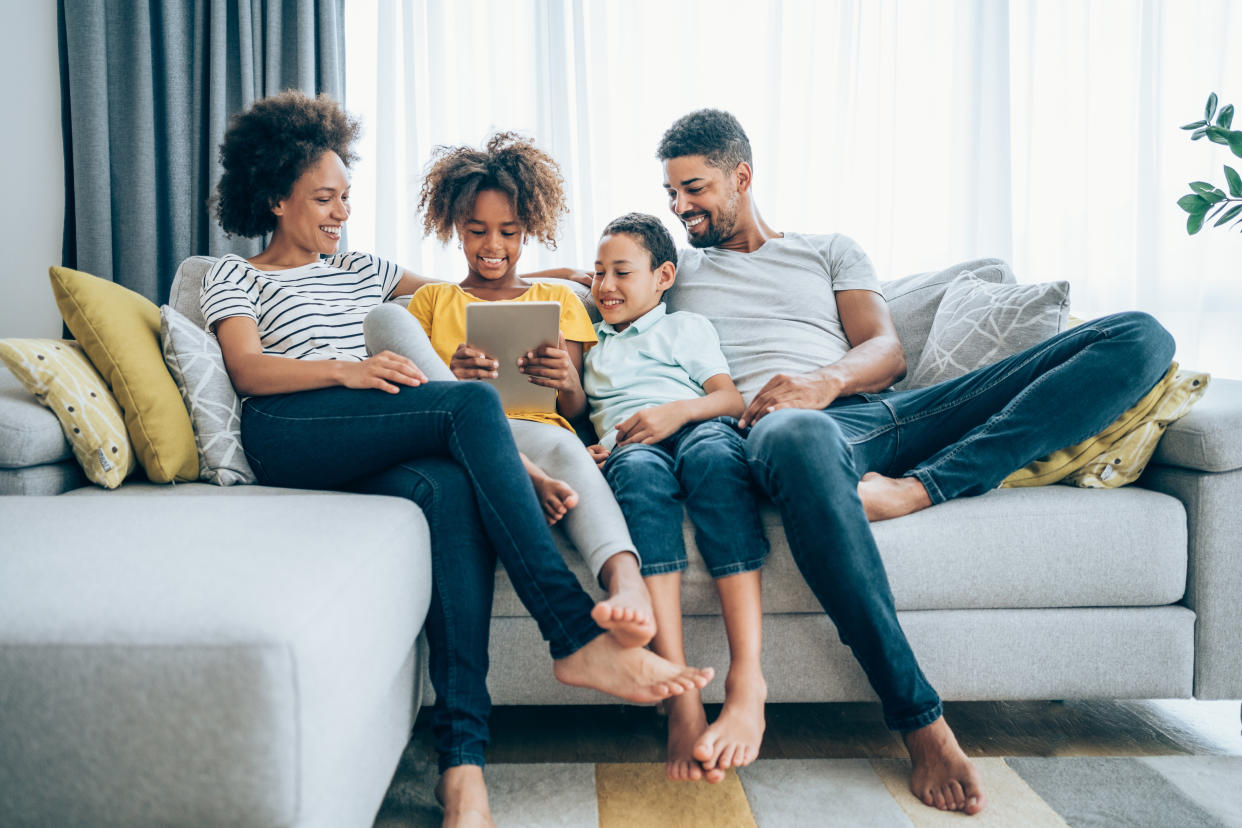 Shot of a smiling family with two kids using digital tablet on the sofa at home.