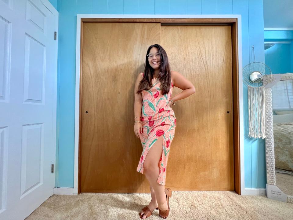 Author wearing long pink dress with flower designs and brown sandals.