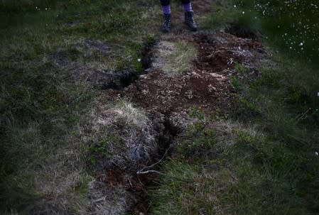 Kathryn Bennett, a postgraduate student in earth science at the University of New Hampshire, stands next to an area of dry, cracked land at a research post at Stordalen Mire near Abisko