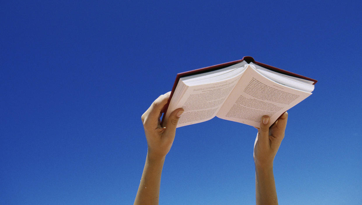 Young woman holding book up in air (Jerome Tisne / Getty Images)