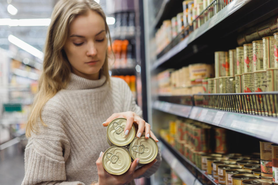 Woman buys stew in cans in a supermarket, provisions and shelf-stable food products