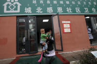 An ethnic minority woman carrying her child leaves a clinic at the apartment houses compound built by the Chinese government in Yuexi county, southwest China's Sichuan province on Sept. 11, 2020. China's ruling Communist Party says such initiatives have helped to lift millions of people out of poverty. But they can require drastic changes, sometimes uprooting whole communities. They fuel complaints the party is trying to erase cultures as it prods minorities to embrace the language and lifestyle of the Han, who make up more than 90% of China's population. The words on top reads: "Preschool speaks Mandarin, not afraid of talking and reading. (AP Photo/Andy Wong)