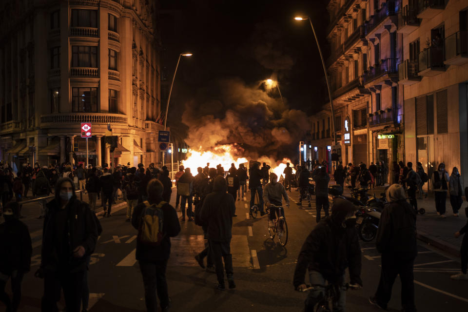 People gather next to a burning barricade during clashes after a protest condemning the arrest of rap singer Pablo Hasél in Barcelona, Spain, Wednesday, Feb. 17, 2021. Police fired rubber bullets and baton-charged protesters as clashes erupted for a second night in a row Wednesday at demonstrations over the arrest of Spanish rap artist Pablo Hasél. Many protesters threw objects at police and used rubbish containers and overturned motorbikes to block streets in both Madrid and Barcelona. (AP Photo/Felipe Dana)