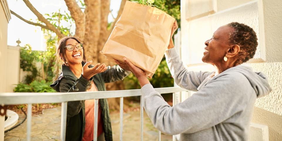 Smiling young woman delivering a bag of groceries to a senior woman outside of her home (weekend work from home jobs) 