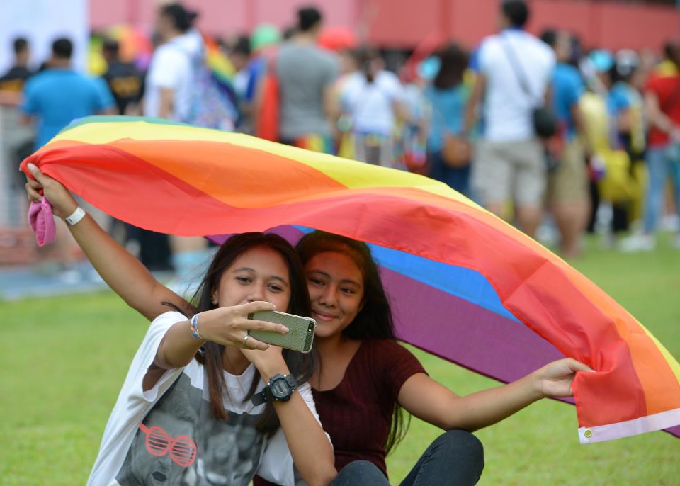 A couple holding a rainbow flag take a selfie as thousands of Lesbian Gay Bisexual Transgender/Transexual Queer (LGBTQ) members hold a pride march at a sports complex in Marikina City, east of Manila on June 30, 2018. - Thousands of gay pride marchers braved heavy rain in Manila on June 30 calling for the legalisation of same-sex marriage as the Philippines' top court considers a landmark legal challenge to the current ban. (Photo by TED ALJIBE / AFP) (Photo credit should read TED ALJIBE/AFP via Getty Images)