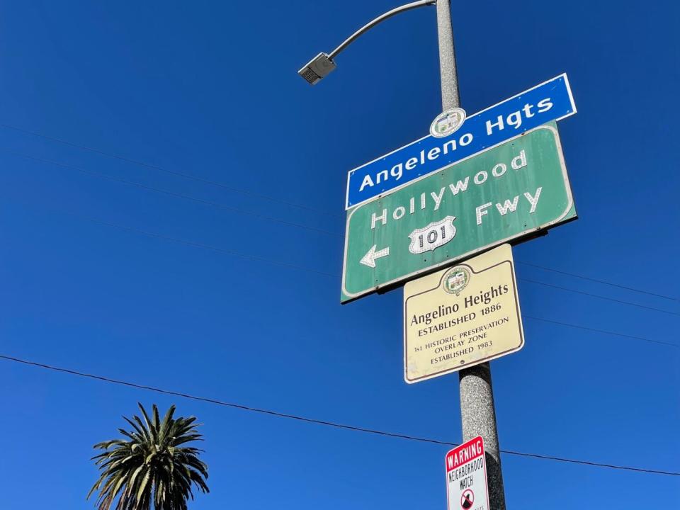 A blue city neighborhood sign spells out "Angeleno Hgts." The historic marker, however, spells it "Angelino Heights."