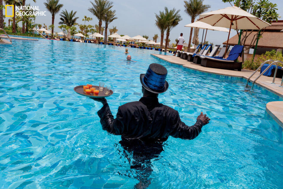 A newly arrived temporary worker from Ghana, on daily duty as “pool ambassador,” attends to thirsty swimmers at Dubai’s five-star Ritz-Carlton hotel.