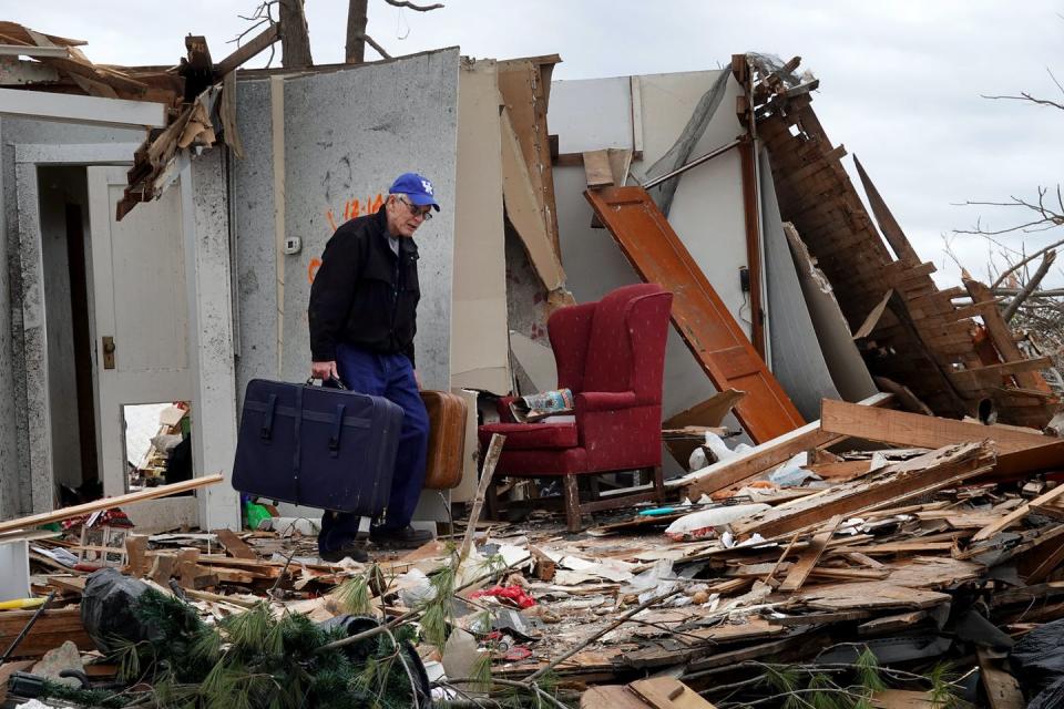 A man carries suitcases out of the shell of a splintered house