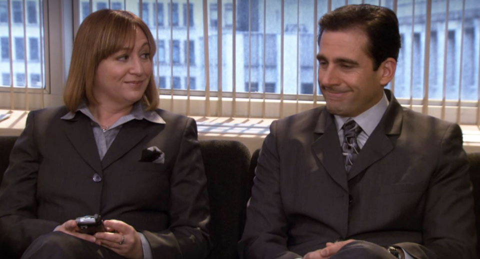 Two characters from "The Office" sitting side by side, smiling slightly, dressed in business attire