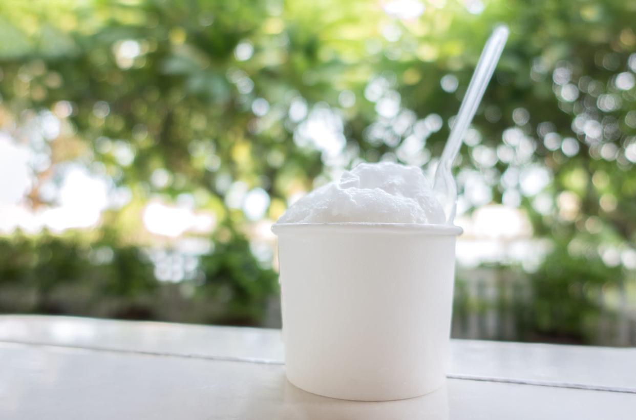 white coconut ice cream in white cardboard  paper tub cup with plastic spoon on white wooden table