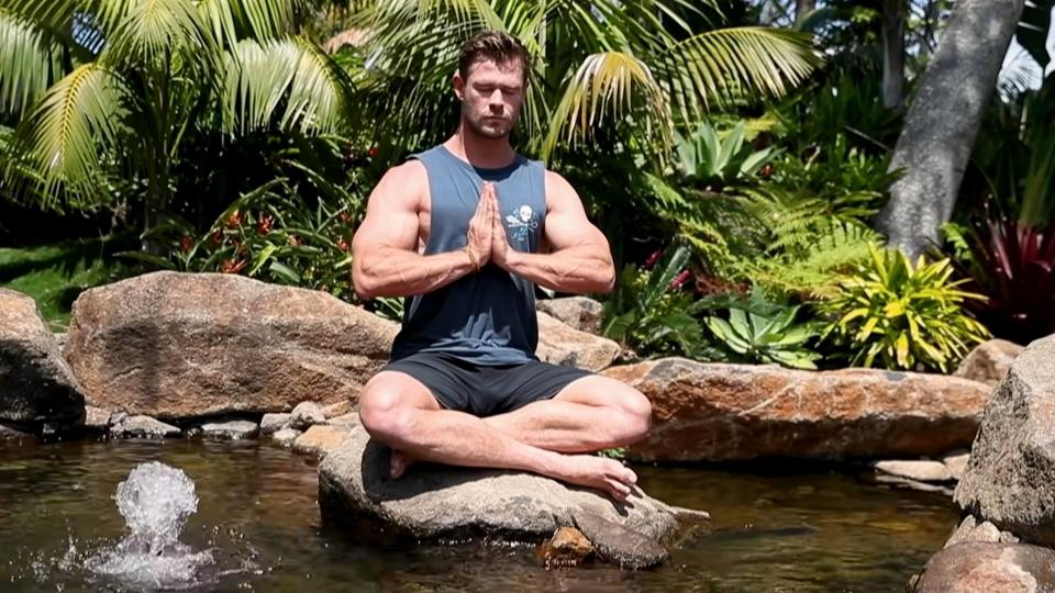 Chris Hemsworth meditating with palms together and legs crossed in a river