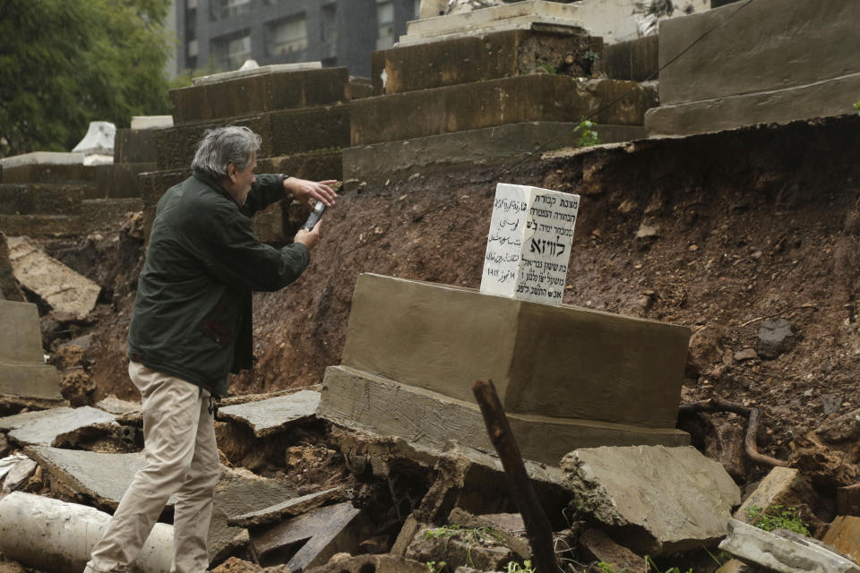 CORRECTS TO CAPITAL'S ONLY JEWISH CEMETERY, NOT COUNTRY'S - A man takes a picture of graves in a Jewish cemetery damaged from heavy rains in the Sodeco area of Beirut, Lebanon, Thursday, Dec. 26, 2019. A heavy storm hit Lebanon with heavy rain and strong winds causing an old wall to collapse in the capital's only Jewish cemetery, causing damage to several tombstones. Lebanon once had a thriving Jewish community, but the various Arab-Israeli wars and Lebanon's own 1975-90 civil war caused waves of emigration and almost none are left in the country today. (AP Photo/Hassan Ammar)