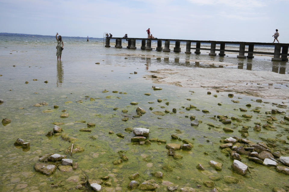 A woman takes a selfie on the peninsula of Sirmione, on Garda lake, Italy, Friday, Aug. 12, 2022. Lake Garda water level has dropped critically following severe drought resulting in rocks to emerge around the Sirmione Peninsula. (AP Photo/Antonio Calanni)