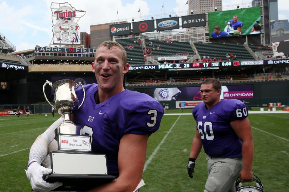 In this Sept. 23, 2017, file photo, St. Thomas wide receiver Tanner Vik walks on the field with the Holy Grail trophy after the team's win over St. John's in an NCAA college football game, in Minneapolis.