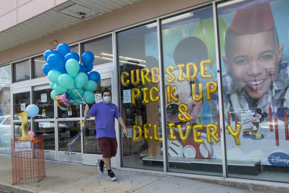 A Party City employee delivers balloons to a customer curbside, Wednesday, May 27, 2020, in Oceanside, N.Y. Long Island has become the latest region of New York to begin easing restrictions put in place to curb the spread of the coronavirus as it enters the first phase of the state's four-step reopening process. (AP Photo/Mary Altaffer)