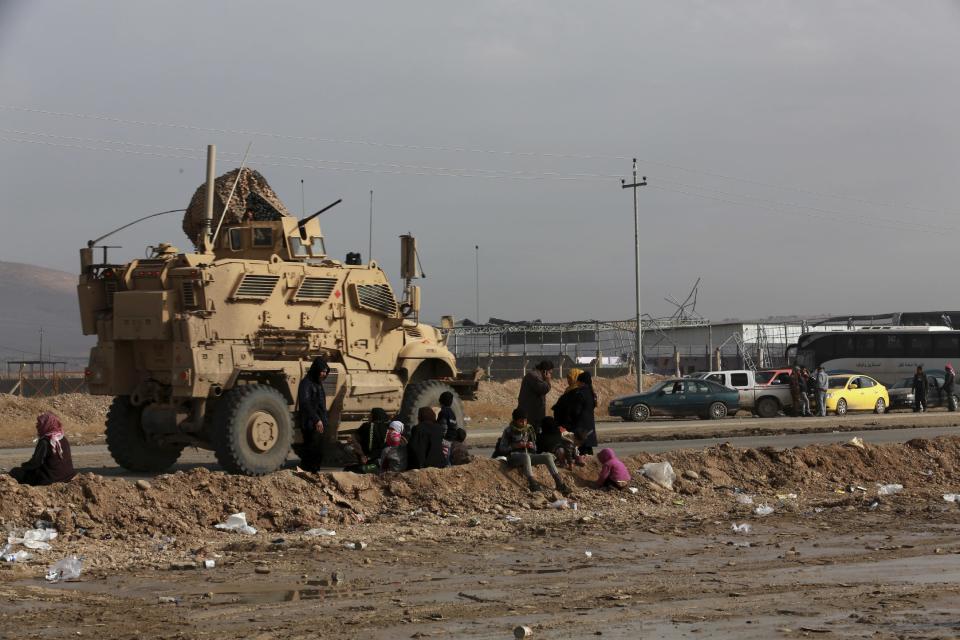 A U.S. Army armoured vehicle passes by displaced Iraqis, who fled fighting between Iraqi security forces and Islamic State militants, in Bartella, around 19 miles (30 kilometers), from Mosul, Iraq, Saturday, Dec 31, 2016. (AP Photo/ Khalid Mohammed)
