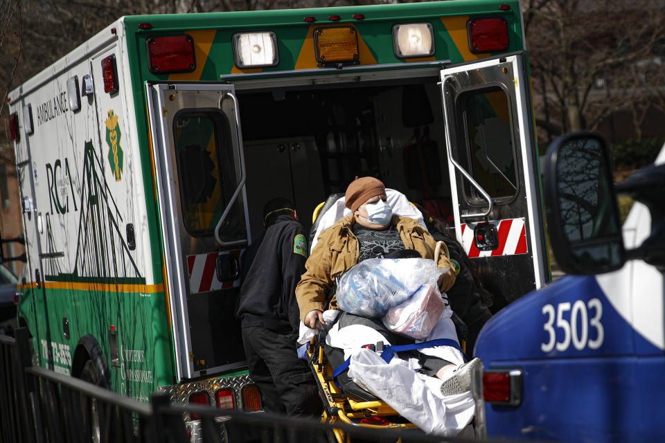 A patient wears a protective face mask as she is loaded into an ambulance at The Brooklyn Hospital Center emergency room, Wednesday, March 18, 2020, in New York. Anticipating a spike in coronavirus patients, New York City-area hospitals are clearing out beds, setting up new spaces to triage patients and urging people with mild symptoms to consult health professionals by phone or video chat instead of flooding emergency rooms that could be overrun. (AP Photo/John Minchillo)