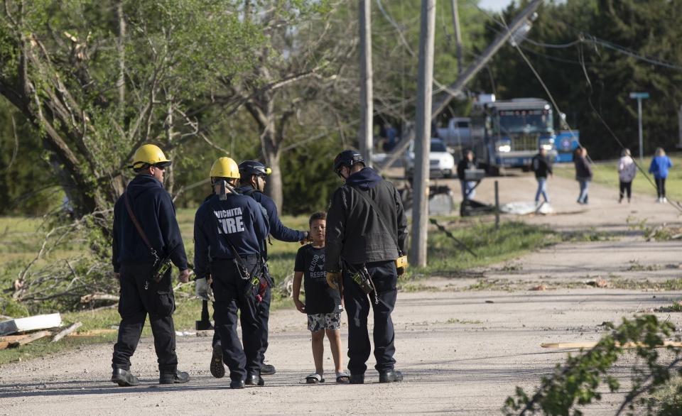 Bomberos de Wichita saludan a Camden Oyewole, de 7 años, mientras realizan una búsqueda en una zona en Andover, Kansas, el sábado 30 de abril de 2022, tras el paso de un devastador tornado. (Jaime Green /The Wichita Eagle vía AP)