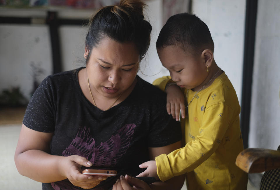 Diana Khumanthem, 30, and her three-year-old nephew Hridhaan looks at photographs on the mobile phone of Hridhaan's mother Ranjita, who died of COVID-19, at home in Imphal, in Manipur, India, Monday, June 28, 2021. Diana lost both her mother and sister to the virus in May. A public hospital treated Diana’s mother, but her sister Ranjita was admitted to a private one that cost $1,300 per day. Ranjita was the family's only earner after Diana left her nursing job last year to return home during the first wave of the virus. She's now hunting for work while looking after her father and her sister’s 3-year-old son. (AP Photo/Yirmiyan Arthur)