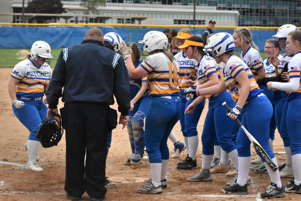 The Mitchell softball team greets Emerie Russell at the plate after the junior deposited a wayward pitch over the fence in left field for a grand slam against Orleans.