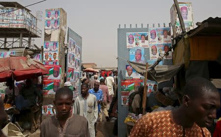 Men walk in front of election posters at an open market in Kano, March 27, 2015. REUTERS/Goran Tomasevic