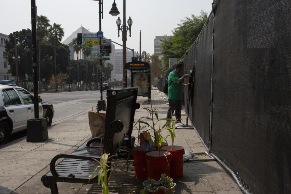 A person stands on a sidewalk near a fence and a metal bench.