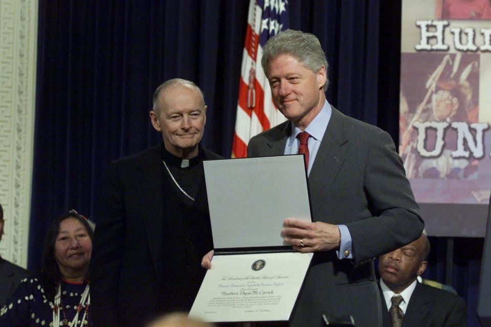 FILE - In this Dec. 6, 2000 file photo, President Bill Clinton presents Archbishop Theodore Edgar McCarrick of Newark, N.J. with a 2000 Eleanor Roosevelt Award for Human Rights during a Human Rights Day ceremony at the Eisenhower Executive Office Building in Washington. On Tuesday, Nov. 10, 2020, the Vatican is taking the extraordinary step of publishing its two-year investigation into the disgraced ex-Cardinal McCarrick, who was defrocked in 2019 after the Vatican determined that years of rumors that he was a sexual predator were true. (AP Photo/Ron Edmonds, File)