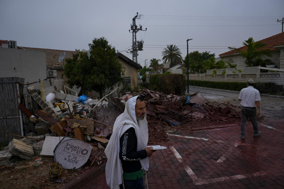 A man covered in a prayer shawl holds a holy book as he stands by a structure destroyed by a rocket fired Wednesday from the Gaza Strip by Palestinian militants, in Ashkelon, Israel, Thursday, May 11, 2023. (AP Photo/Ariel Schalit)