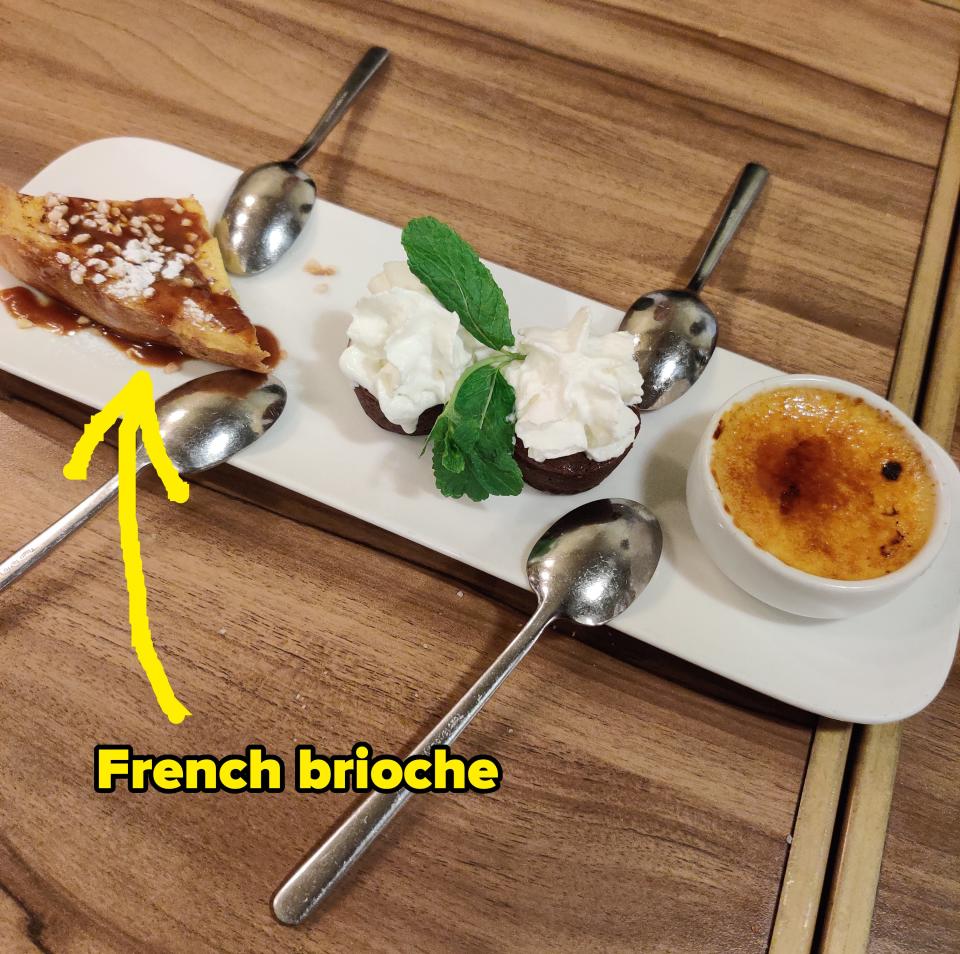 A dessert platter featuring caramel-topped pastry, whipped cream with mint leaves, and a small creme brulee with four spoons on a wooden table